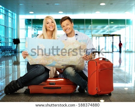 Young couple with map sitting on suitcases in airport