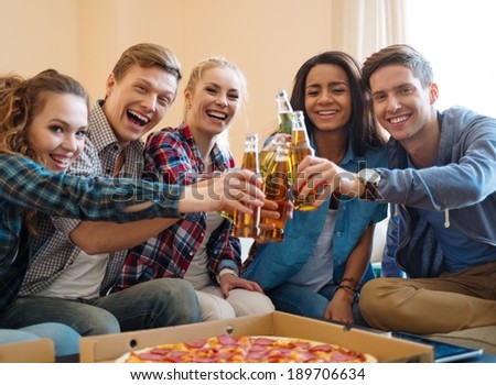 Group of young friends with pizza and bottles of drink celebrating in home interior
