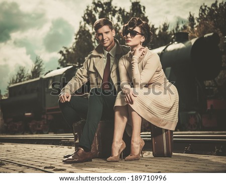 Beautiful vintage style couple sitting on suitcases on  train station platform
