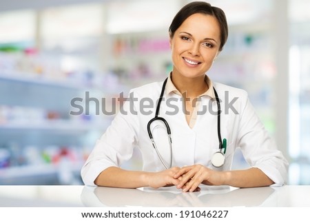 Young positive brunette doctor woman behind table in drug store