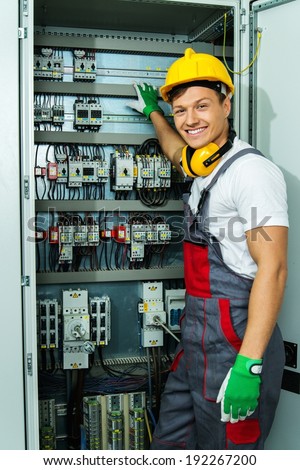 Cheerful electrician in a safety hat on a factory
