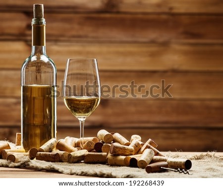 Bottle and glass of white wine on a wooden table among corks