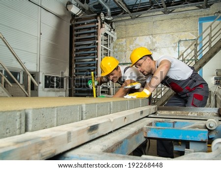 Worker and foreman in a safety hats performing quality check on a factory