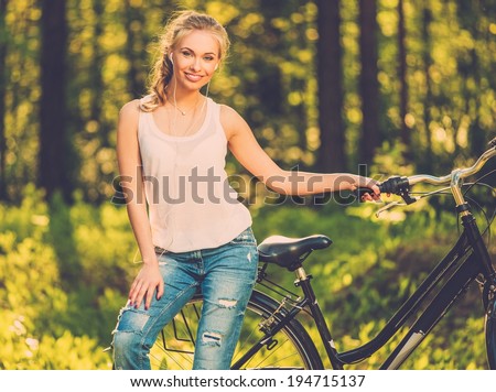 Beautiful teenage girl listens music on bicycle outdoors