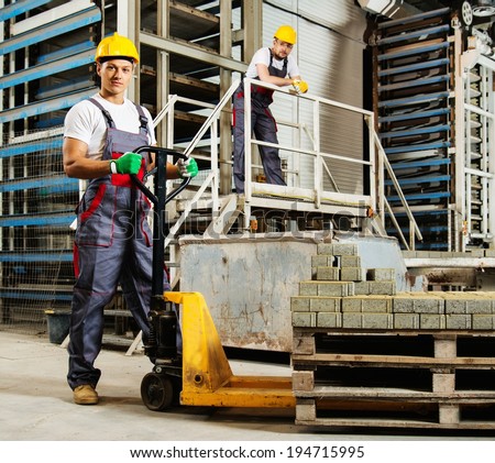 Young worker moving paving stones with pallet truck on a factory