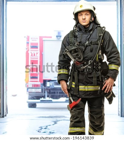 Young firefighter against truck in firefighting depot