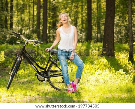 Smiling teenage girl with bicycle in a park on sunny day