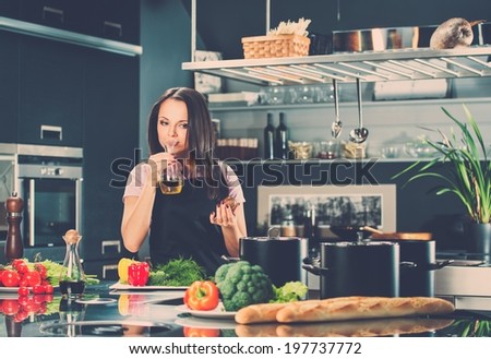 Young woman in apron on modern kitchen smelling olive oil