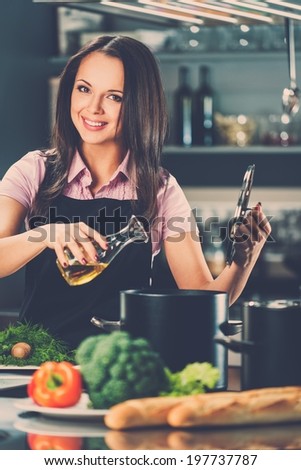 Smiling young woman adding oil to pot on a modern kitchen