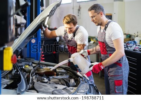 Two mechanics adding oil level in a car workshop