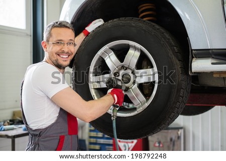 Cheerful serviceman unscrewing wheel in car workshop