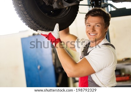 Cheerful serviceman checking suspension in a car workshop