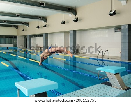 Young muscular swimmer jumping from starting block in a swimming pool