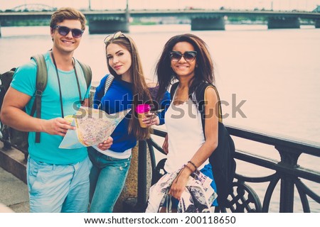 Multi-ethnic friends tourists with map and coffee cups near river in a city