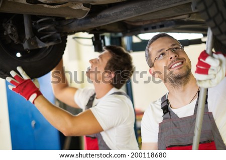 Servicemans checking suspension in a car workshop