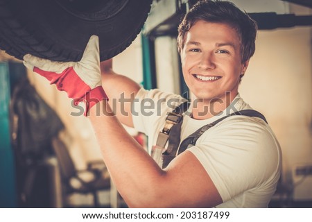 Cheerful serviceman checking suspension in a car workshop