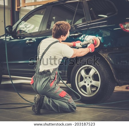 Serviceman polishing car body with machine  in a workshop