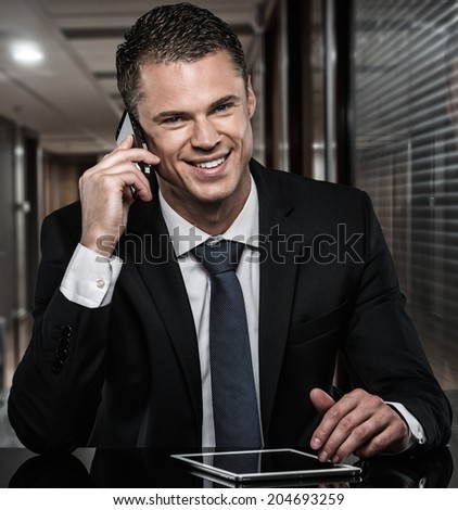 Handsome man in black suit with mobile phone and tablet pc in modern office