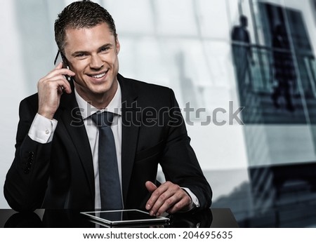 Handsome man in black suit with mobile phone and tablet pc in modern office