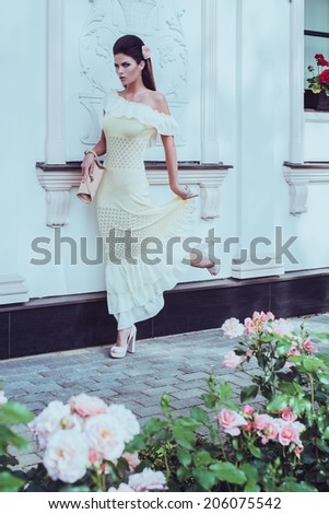 Beautiful woman in dress near luxury building facade among roses