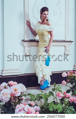 Beautiful woman in dress near luxury building facade among roses