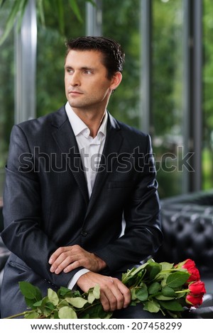 Handsome man with bunch of red roses waiting his lady in restaurant
