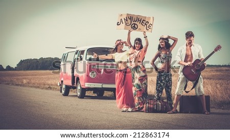 Multi-ethnic hippie hitchhikers with guitar and luggage on a road