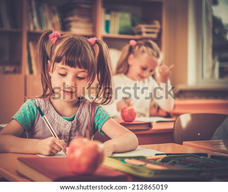 Little schoolgirl sitting behind school desk during lesson in school