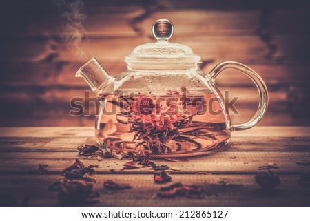 Glass teapot with blooming tea flower inside against wooden background