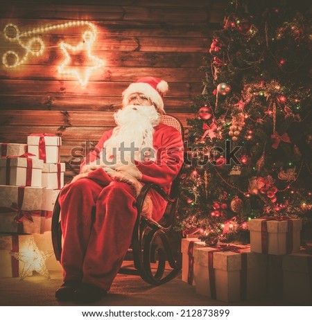 Santa Claus sitting on rocking chair in wooden home interior with illuminated decoration on a wall