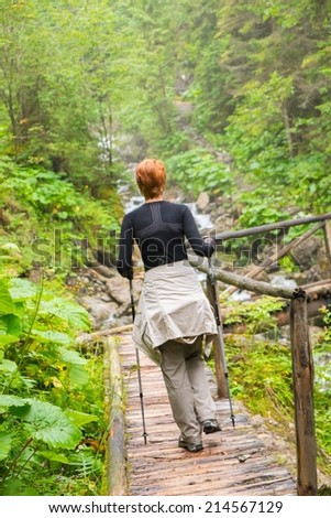 Hiker with hiking poles looking walking over wooden bridge in a forest