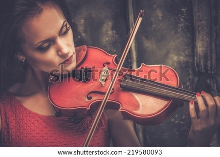 Young woman in red dress playing violin in mystic interior