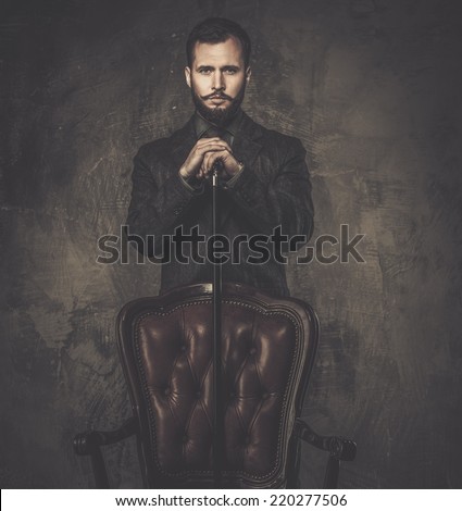 Handsome well-dressed man with stick standing near leather chair