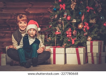 Mother and lIttle boy with gift box under christmas tree in wooden house interior