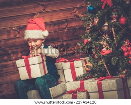 Little boy with gift box under christmas tree in wooden house interior