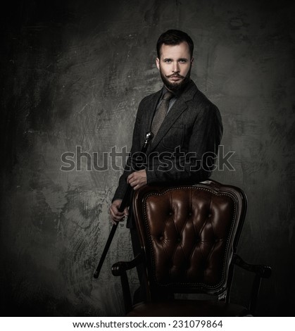 Handsome well-dressed man with stick standing near leather chair