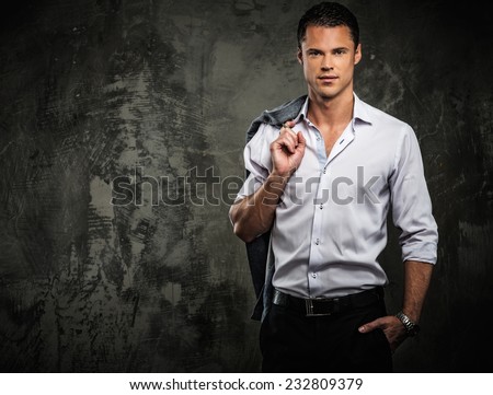 Handsome man in shirt against grunge wall holding jacket over shoulder