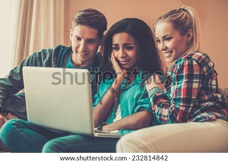 Three young students with laptop  in home interior