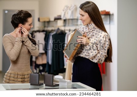 Young woman choosing jewellery with shop assistant  help