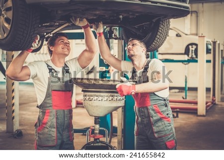 Two mechanics changing oil  in a car workshop