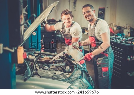 Two mechanics adding oil level in a car workshop
