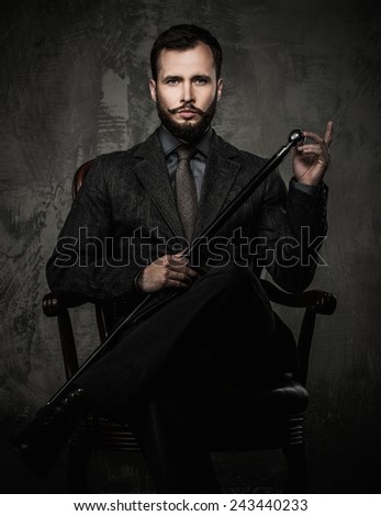 Handsome well-dressed man with walking stick sitting in leather chair