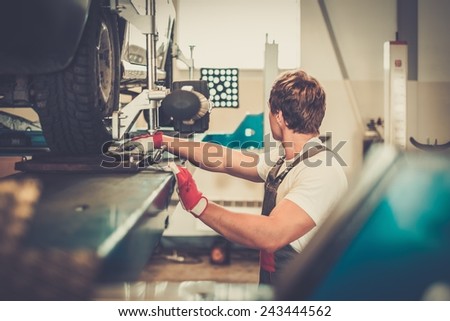 Young serviceman checking wheel alignment  in a car workshop