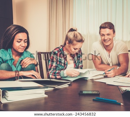 Multi ethnic group of students preparing for exams in home interior behind table