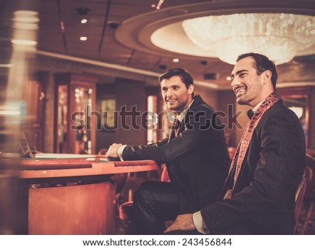 Two fashionable men in suits behind table in a casino
