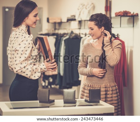 Young woman choosing jewellery with shop assistant  help