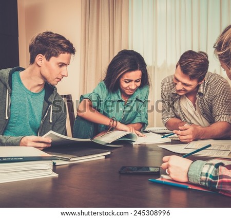Multi ethnic group of students preparing for exams in home interior behind table
