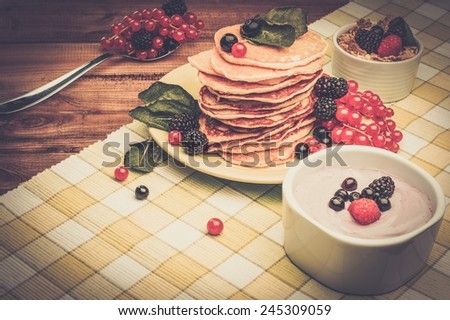 Healthy breakfast with pancakes, fresh berries and yoghurt on tablecloth in rural interior