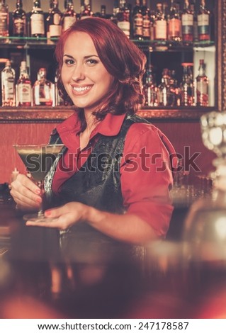 Beautiful redhead barmaid with cocktail behind bar counter