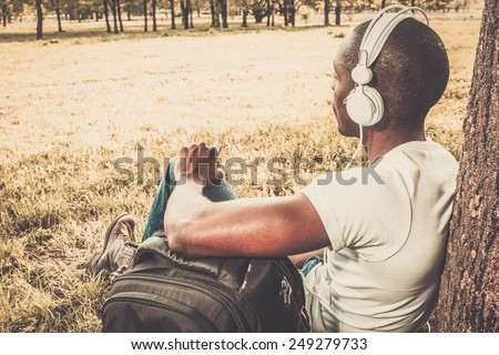 Smiling young african american man listens music in a park